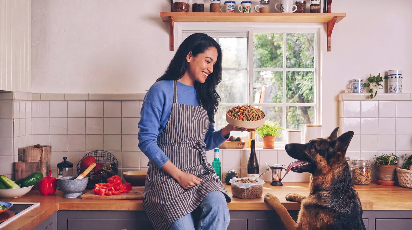 Mujer sirviendo comida natural Bone Appetit a su perro en la cocina